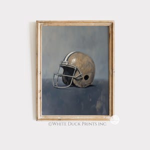 Peut inclure: Impression d'art encadr&eacute;e d'un casque de football am&eacute;ricain. Le casque est brun clair avec une bande blanche et un masque facial argent&eacute;. Le fond est un m&eacute;lange de tons bleus et gris, et le cadre est en bois clair.