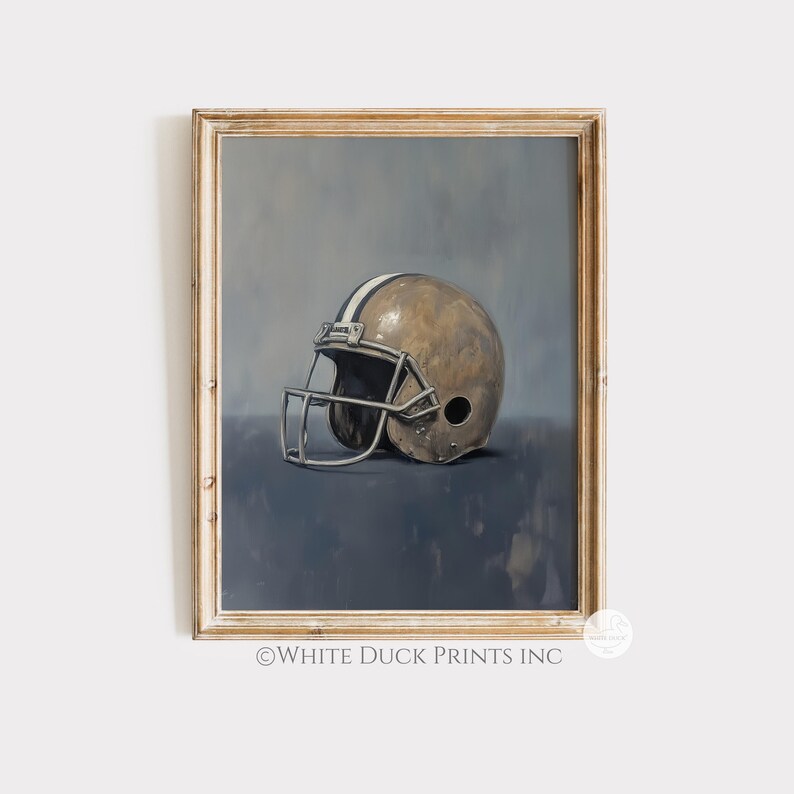 Peut inclure: Impression d'art encadr&eacute;e d'un casque de football am&eacute;ricain. Le casque est brun clair avec une bande blanche et un masque facial argent&eacute;. Le fond est un m&eacute;lange de tons bleus et gris, et le cadre est en bois clair.