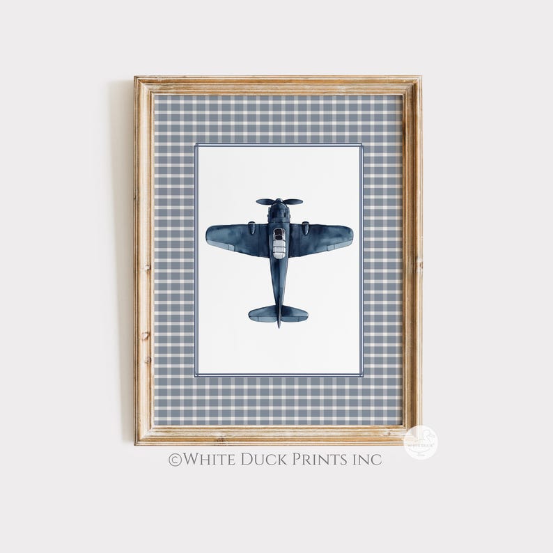 Puede incluir: Una impresi&oacute;n enmarcada con una ilustraci&oacute;n en acuarela de un avi&oacute;n azul marino. La obra de arte est&aacute; sobre un fondo blanco dentro de un borde a cuadros azul y un marco de madera. La impresi&oacute;n es una pieza decorativa.