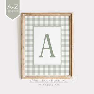 Pode incluir: Uma impressão emoldurada com a letra "A" em um tom verde suave. O fundo apresenta um padrão xadrez vichy verde claro e branco. A moldura de madeira adiciona um toque rústico. O texto "A-Z INCLUDED" está no canto superior esquerdo.