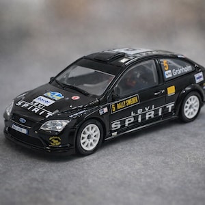 May include: A black Ford Focus rally car model with white wheels and the text "Levi Spirit" on the side. The car has sponsor decals and the number 5 on the side. The car is on a grey surface.