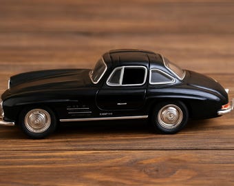 Op de afbeelding: Een zwart vintage automodel met zilveren accenten, waaronder de wielen en bumpers. De auto heeft een gestroomlijnd ontwerp en staat op een houten achtergrond. Het model is een klassieke auto.