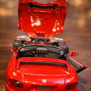 Puede incluir: Un coche de juguete rojo con el capó y la puerta abiertos, revelando el motor y los detalles interiores. El coche es un modelo descapotable, con un salpicadero detallado y un diseño elegante. Es una réplica en miniatura.