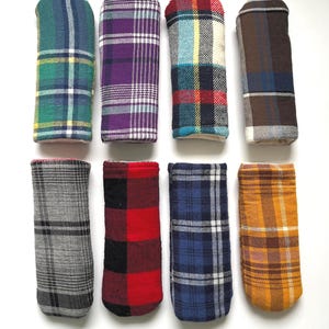 May include: Eight rectangular fabric covers arranged in two rows of four. Each cover features a distinct plaid or tartan pattern in various colors including green, purple, red, blue, grey, black, and yellow, with visible stitching along the edges.