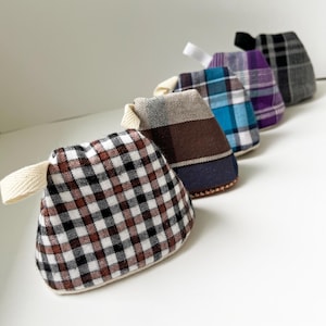 Puede incluir: Una fila de cinco pequeñas bolsas de tela triangulares con patrones de cuadros en blanco y negro, marrón y beige, azul y blanco, morado y blanco, y negro y gris. Cada bolsa cuenta con una pequeña presilla de tela en una esquina.