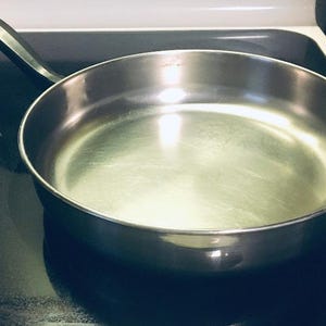 May include: A silver frying pan with a black handle on a black stovetop.