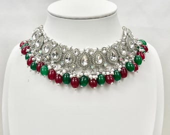 May include: A silver choker necklace with a teardrop-shaped design and clear rhinestones. The necklace has a double row of green and red beads.
