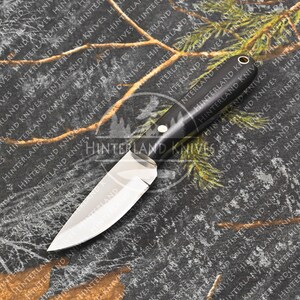 May include: A small, black-handled knife with a silver blade. The knife is lying on a camouflage fabric background.