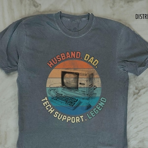 May include: Gray t-shirt with a retro computer graphic and the words "HUSBAND. DAD. TECH SUPPORT. LEGEND" in a circular design. The shirt has a distressed vintage look.