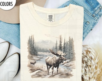 May include: A cream colored t-shirt with a brown moose illustration in a forest setting. The text "COMFORT COLORS" is on the tag.
