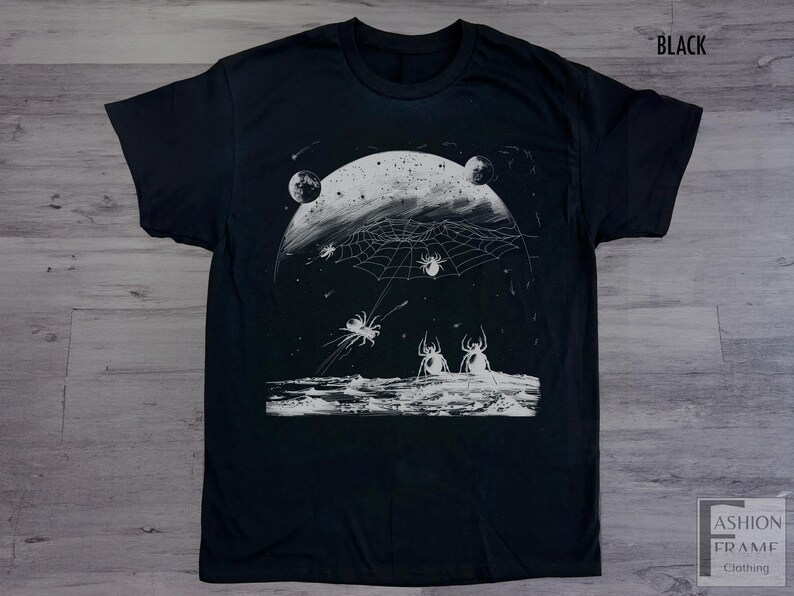 以下が含まれることがあります： 月のクモの巣とクモの白いグラフィックプリントが施された黒いTシャツ。グラフィックはヴィンテージスタイルです。