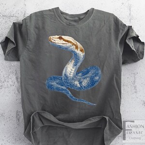 May include: Gray t-shirt featuring a detailed illustration of a snake. The snake's head is brown and tan, while its body is a blue wireframe design. The shirt has short sleeves and a crew neck.