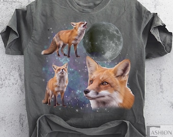 May include: A gray t-shirt featuring a design with three foxes, a full moon, and a starry background. The foxes are depicted in shades of orange and white. The shirt has a vintage, worn look.