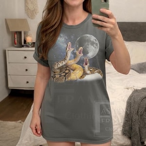 May include: Gray t-shirt featuring a graphic of three snakes with open mouths, a full moon, and a starry sky background. The snakes are in shades of brown, tan, and yellow. The shirt is a casual, short-sleeved style.