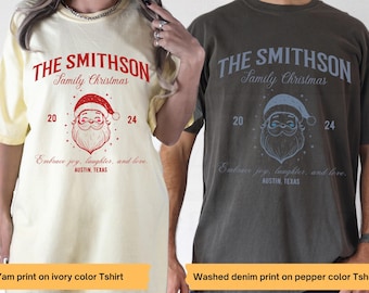 May include: Two t-shirts with a Christmas theme. The ivory t-shirt has a red Santa Claus graphic and the text "THE SMITHSON Family Christmas 20 24 Embrace joy, laughter, and love. AUSTIN, TEXAS". The pepper color t-shirt has a blue Santa Claus graphic and the same text in blue.