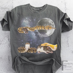 May include: Dark gray t-shirt featuring a surreal design with a full moon, snakes, and rats. The snakes are patterned in brown and yellow, and the rats are gray and white. The design is set against a starry night sky.