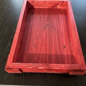 May include: A rectangular wooden tray with a deep red stain. The tray has a simple design with a smooth, polished finish.