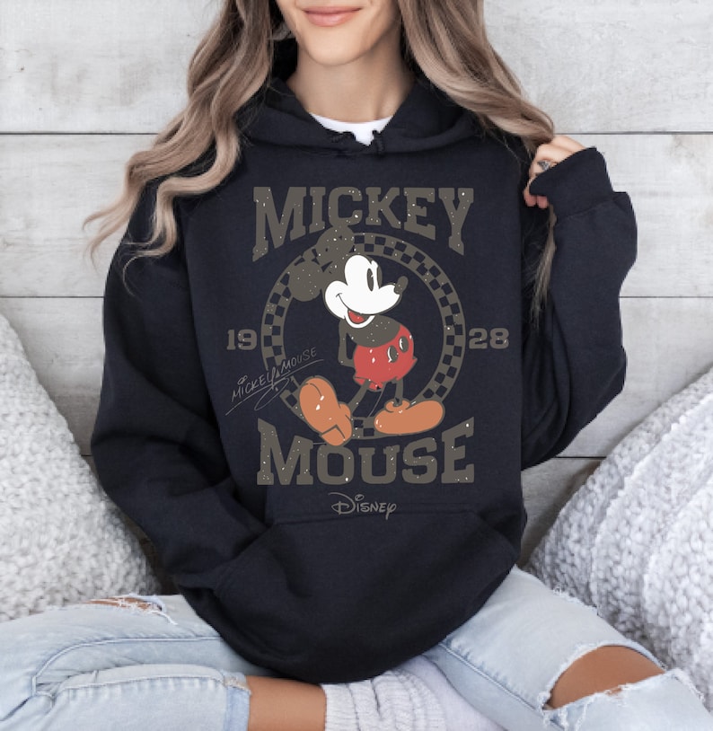 May include: Black hooded sweatshirt featuring a distressed graphic of Mickey Mouse. The design includes the words "Mickey Mouse" and "Disney" along with the years "1928" and "1928". The graphic is in shades of brown, white, red, and black.