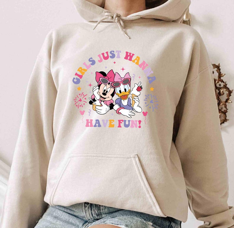May include: A beige hoodie with a graphic print of Minnie Mouse and Daisy Duck wearing sunglasses and holding ice cream cones. The text "Girls Just Wanna Have Fun!" is printed in a rainbow arc above the characters.