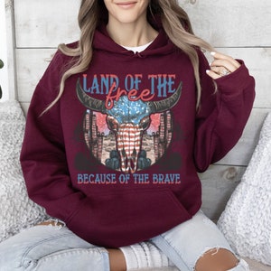 May include: Burgundy hooded sweatshirt with a graphic of a skull with an American flag design and the text "Land of the free because of the brave".