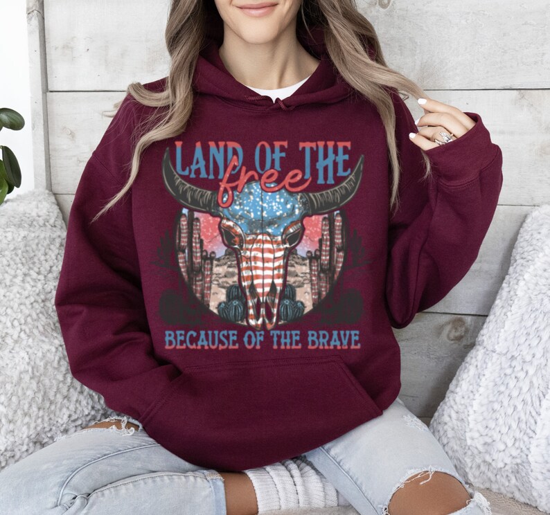May include: Burgundy hooded sweatshirt with a graphic of a skull with an American flag design and the text "Land of the free because of the brave".