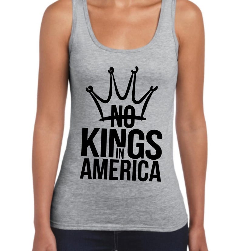 May include: A grey vest top featuring a black crown design and the words "NO KINGS IN AMERICA". The top has a scoop neck and is sleeveless. The graphic is printed in the centre.