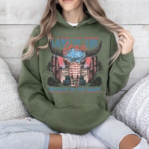 May include: Green hooded sweatshirt with a graphic print of a skull with an American flag design. The text "Land of the Free Because of the Brave" is printed below the skull.