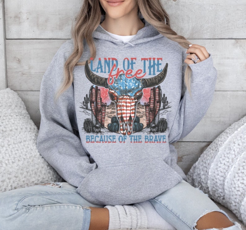May include: Gray hooded sweatshirt with a graphic print of a bull skull with an American flag design. The text "Land of the free because of the brave" is printed below the skull.