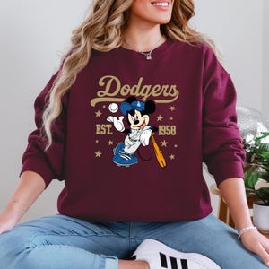 May include: A white ceramic mug with a black handle and the text "But First, Coffee" in a bold, black font. The mug is set against a blurred background. The mug appears to be approximately 10 cm tall.