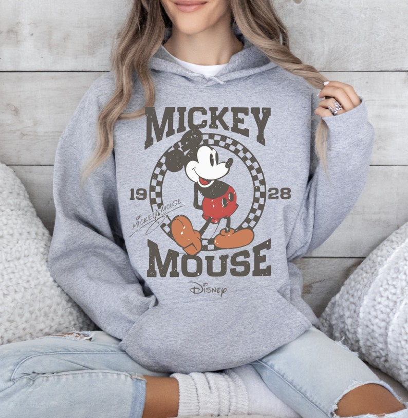 May include: A gray hooded sweatshirt featuring a vintage Mickey Mouse graphic. The design includes the words "Mickey Mouse" and the year "1928" in a circular frame. The Disney logo is at the bottom of the graphic.