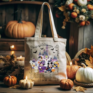 May include: Beige canvas tote bag featuring a Halloween-themed Disneyland design. The graphic includes cartoon characters in costumes, a castle, bats, and the Disneyland logo. Pumpkins and candles surround the bag.