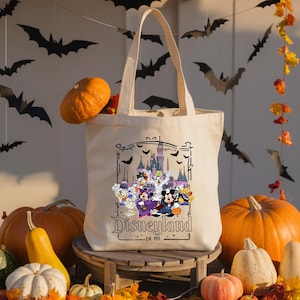 May include: A cream-colored tote bag featuring a Disneyland Halloween design with Mickey Mouse, Minnie Mouse, and other Disney characters in costume. The bag is surrounded by pumpkins and fall decorations.