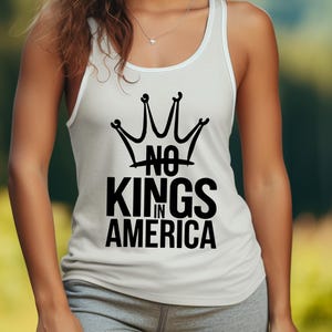 May include: White vest top featuring a black crown design and the words "NO KINGS IN AMERICA". The top has a scoop neckline and white trim. The text is in a bold, sans-serif font.