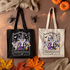 May include: Two tote bags, one black and one off-white, featuring a Disneyland Halloween design. The design includes cartoon characters, a castle, bats, and the text "Disneyland Est. 1955". Decorative spiders and pumpkins are also present.