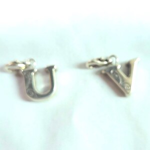 May include: Four silver-colored alphabet charms: T, U, V, and W. Each charm has a small loop at the top for attaching to a chain or bracelet. The letters have a decorative design.