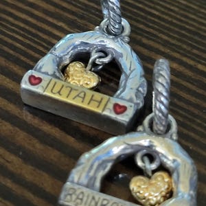 Puede incluir: Dos colgantes plateados con un dije de coraz&oacute;n dorado. Uno dice "UTAH" y el otro "RAINBOW BRIDGE". Ambos tienen un dise&ntilde;o de arco plateado con detalles de coraz&oacute;n rojo. Para collares o pulseras.