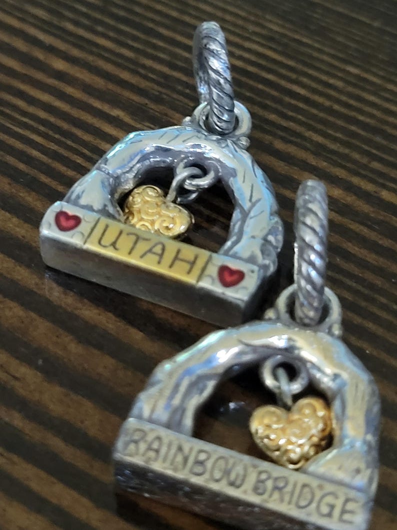 Puede incluir: Dos colgantes plateados con un dije de coraz&oacute;n dorado. Uno dice "UTAH" y el otro "RAINBOW BRIDGE". Ambos tienen un dise&ntilde;o de arco plateado con detalles de coraz&oacute;n rojo. Para collares o pulseras.