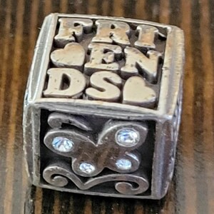 May include: A silver-toned, rectangular charm with the word "FRIENDS" in raised letters. The charm features heart accents and a butterfly design with clear crystal embellishments, perfect for a bracelet or necklace.