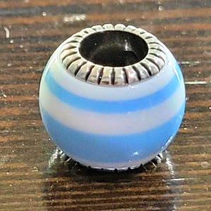 May include: A round bead with a silver-colored top and a blue and white striped design. The bead has a hole through the center and is likely used for jewelry making or as a decorative element.