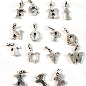 May include: A collection of silver-toned alphabet charms, each with a decorative swirl design. The charms are suspended from small silver loops, and are arranged on a white background. The letters include F, G, H, I, N, O, P, Q, T, U, V, W, X, Y, and Z.