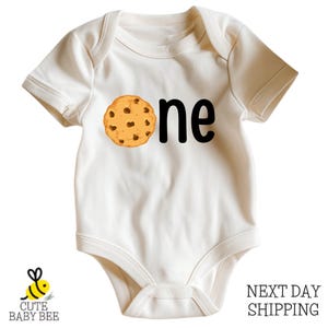A white baby onesie with a cookie graphic printed on it.