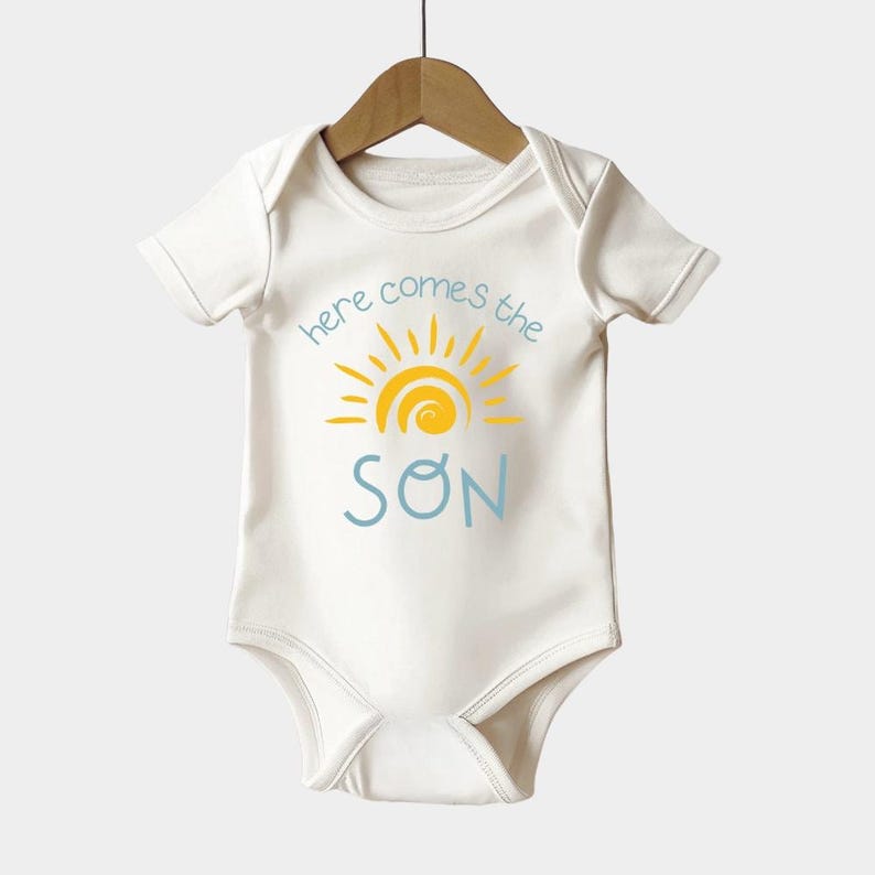a baby's bodysuit with the words here comes the son on it