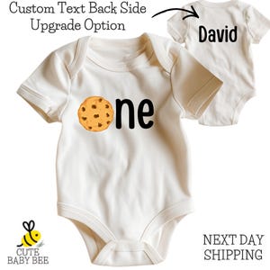 A white baby onesie with a cookie-themed design, featuring the text "One" and the name "David" printed on it.