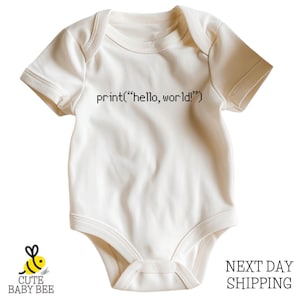 May include: Cream-colored baby onesie with short sleeves. The text "print("hello, world!")" is printed in black across the front. A small yellow bee logo is in the lower left corner. The onesie is made of soft material.