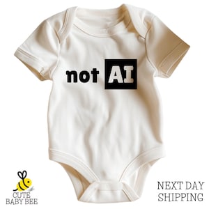 May include: A short-sleeved, off-white baby bodysuit featuring the black text 'not AI' printed across the chest. The letters 'AI' are enclosed within a solid black square. The garment has a round neckline and ribbed trim at the sleeve openings.
