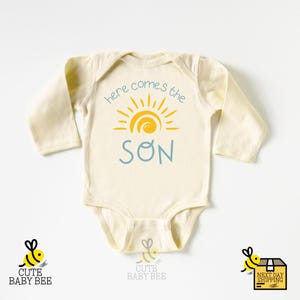 a baby bodysuit with the words here comes the son on it