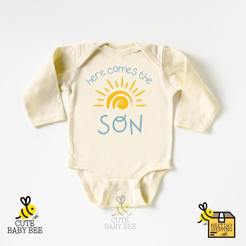 a baby bodysuit with the words here comes the son on it