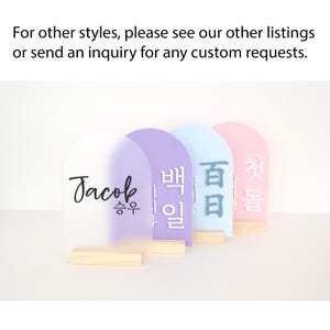 Puede incluir: Cuatro letreros acr&iacute;licos coloridos con bases de madera. Los letreros son en tonos de blanco, morado, azul y rosa. Cada letrero tiene texto en una fuente diferente. El texto en el primer letrero dice "Jacob" y "승우".