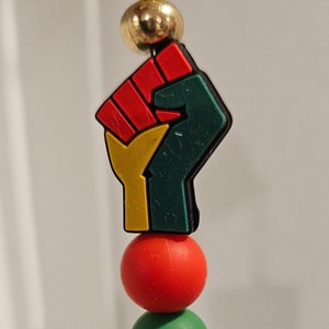 May include: A beaded keychain with a raised fist charm in red, yellow, and green colors. The keychain also features black and green beads.