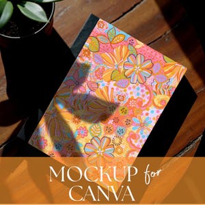 May include: A notebook featuring a vibrant floral design in orange, pink, yellow, and blue hues. The words "MOCKUP for CANVA" are at the bottom. The notebook rests on a wooden surface.